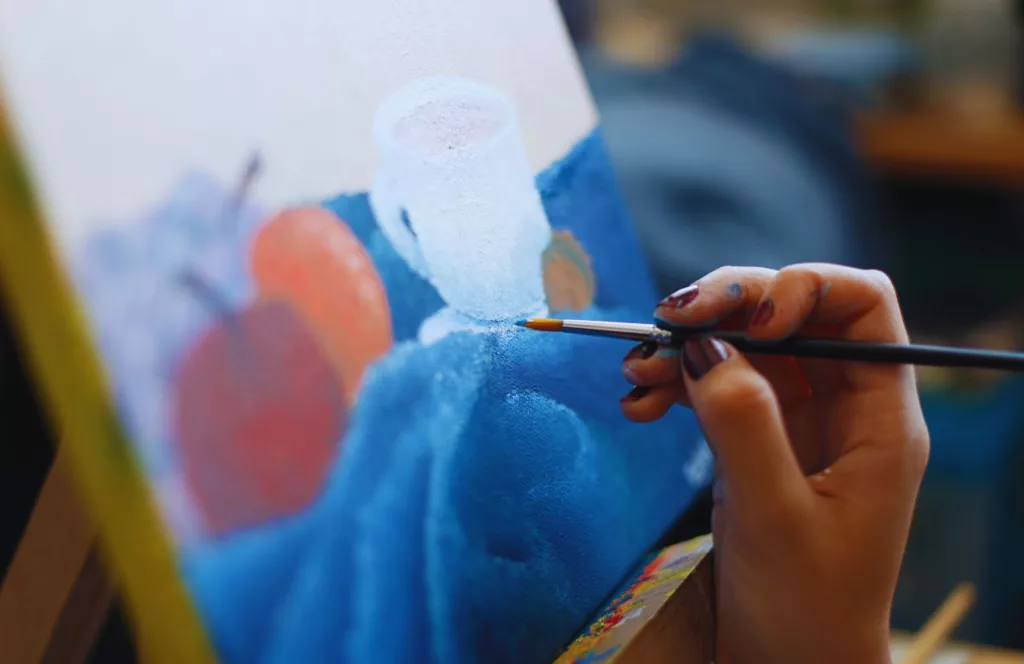 Female with a small paintbrush in her hand with blue paint, painting a canvas at Disney World. Keep reading to find out the best things to do at Disney World for adults.