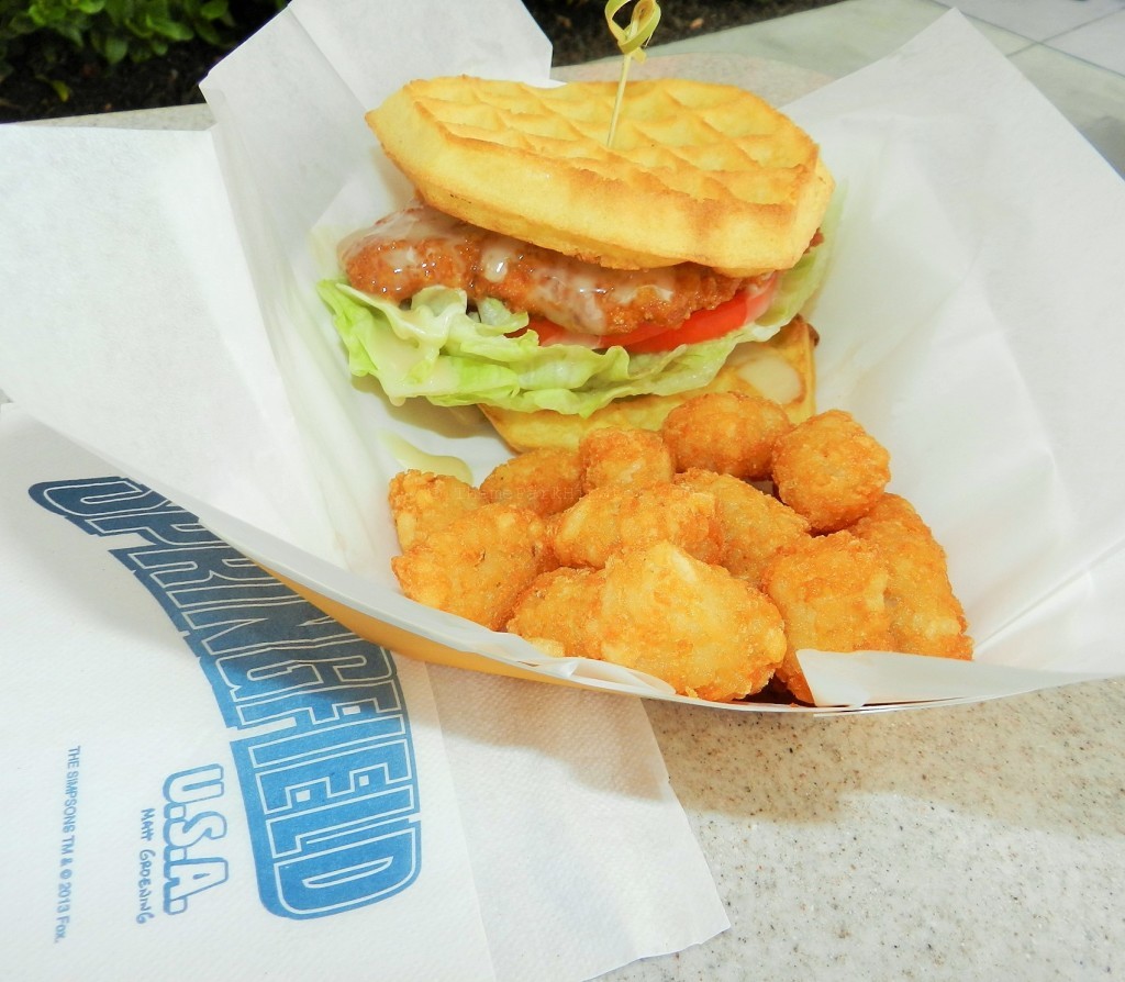 Crunchy golden Chicken and Waffle Sandwich from Cletus' Chicken Shack with glaze maple syrup mayo on a bed of bright green lettuce and red tomatoes.