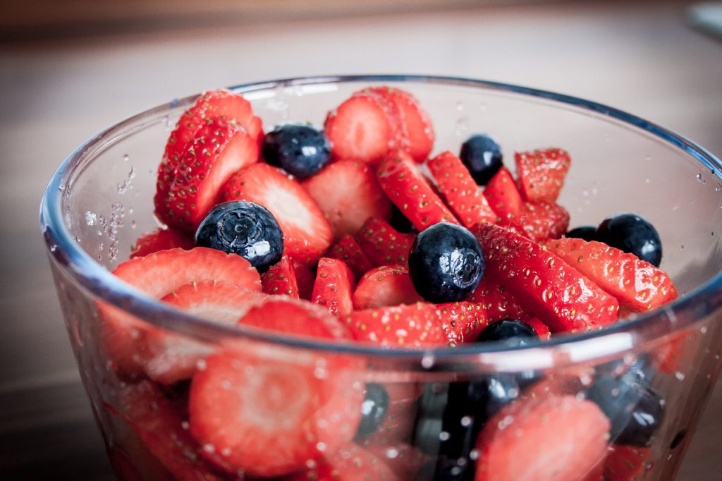 Red strawberries and blueberries in a clear bowl.