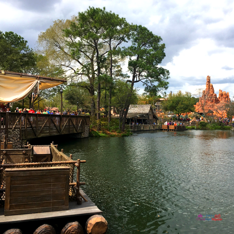 Tom Sawyer Island at Magic Kingdom with raft on water and Big Thunder Mountain Railroad in the background. Disney Secrets. #MagicKingdom #DisneyTips #DisneyPlanning #Disney