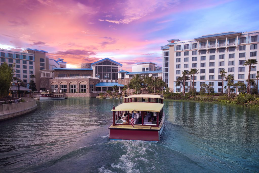 Loews Sapphire Falls Water Taxi saling against the backdrop of Loews Sapphire Falls Resort and sunset. Keep reading to discover what are the best lounges at Universal Orlando.