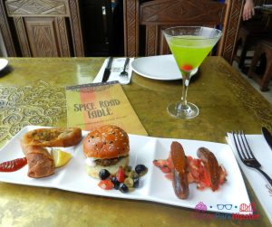 Spice Road Table at Epcot Lamb Sausage and Lamb Slider on White Plate with Green Martini