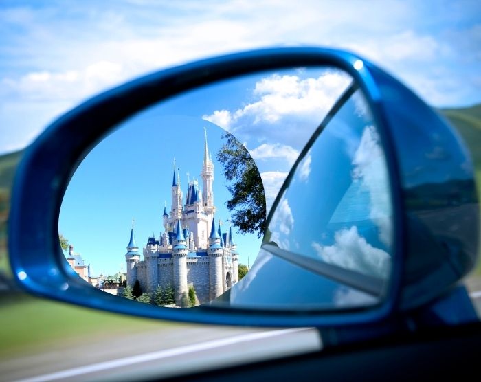 Road Trip to Disney World in Orlando with magic kingdom cinderella castle in rear view window of car. Keep reading to learn how to fly to Orlando and how to find cheap flights to Orlando.