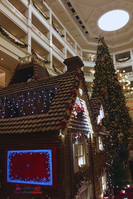 Disney Grand Floridian Gingerbread house with Christmas Tree in background. Keep reading to learn about the best Disney Resorts at Christmas!