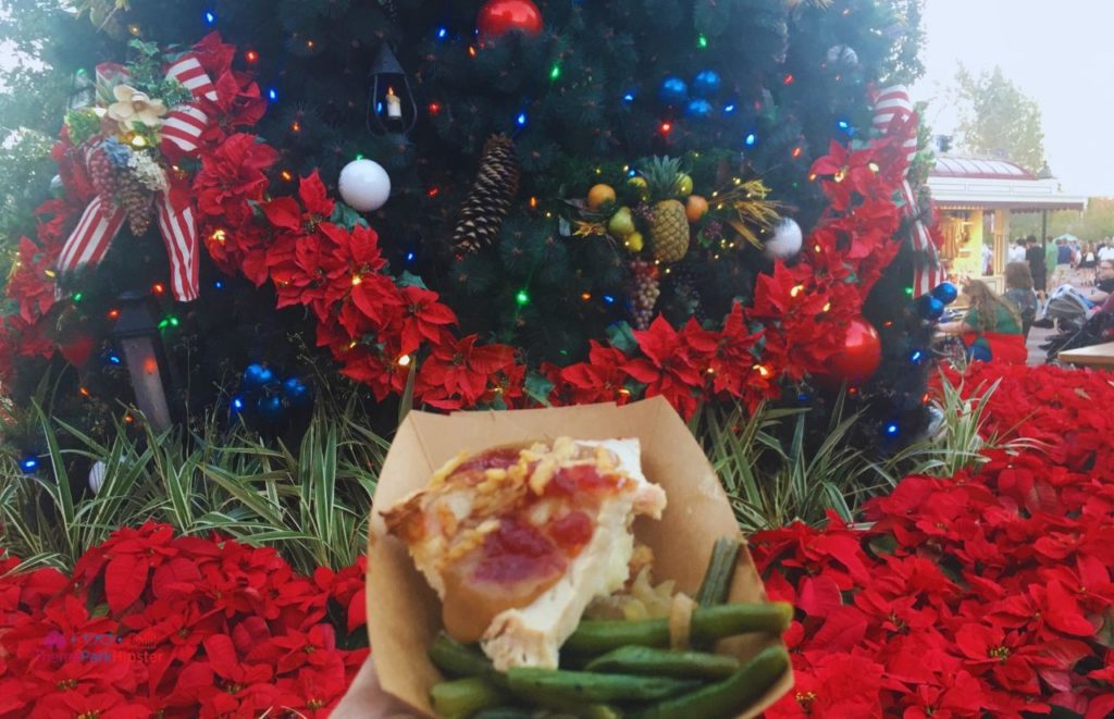 Epcot Festival of the Holidays Christmas Food Turkey Dinner in front of Christmas Tree. One of the best Disney world Christmas snacks.