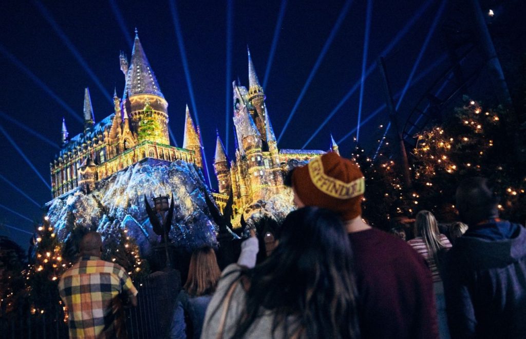 Couple cuddling while watch the luminous Hogwarts for Christmas Lights Show in Hogsmeade Wizarding World of Harry Potter. Keep reading to to find out more Mistakes to Avoid at Universal Orlando Resort!