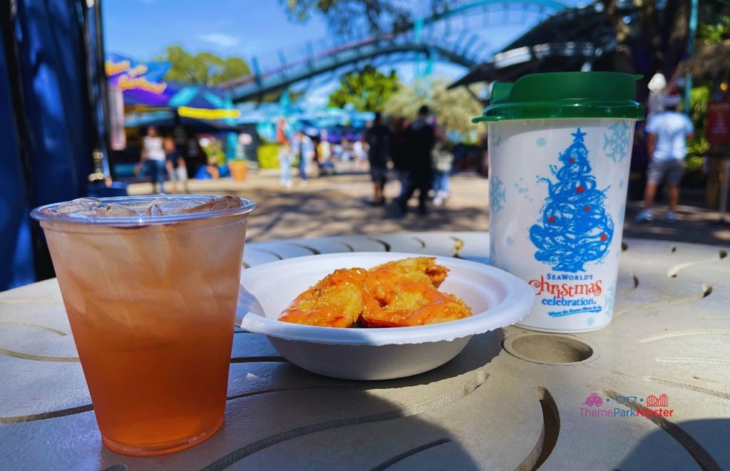 SeaWorld Christmas Celebration Red Holiday Cocktail and Shrimp in front of Mako Roller Coaster. Keep reading to learn about the SeaWorld Annual Pass and Pass Member Perks and Benefits.