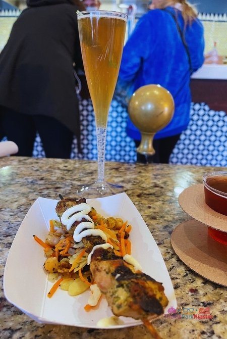 Epcot International Festival of the Arts 2023 Tangerine Cafe Chicken Skewers and Chai Tea Mimosa Morocco. Keep reading to get the full Epcot Festival of the Arts guide, tips, food, concerts and more!