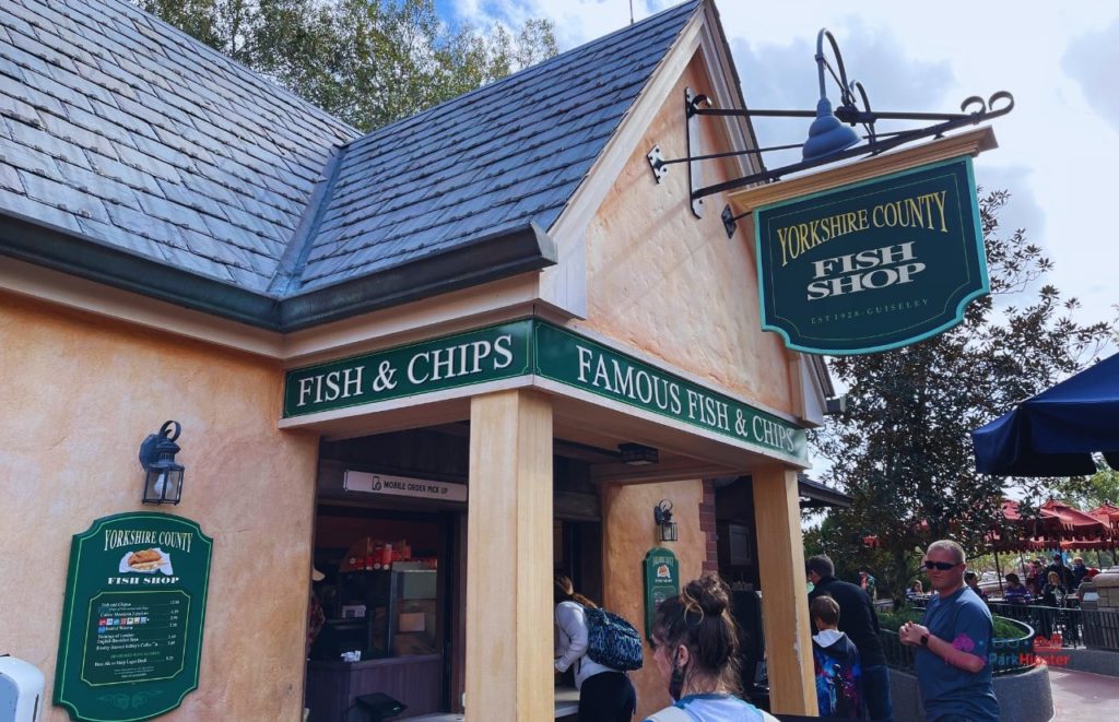 EPCOT theme park guests standing at the to go window at Rose and Crown Yorkshire County Fish and Chips Shop at Disney Epcot. Keep reading to find out the top 10 best snacks at EPCOT. 