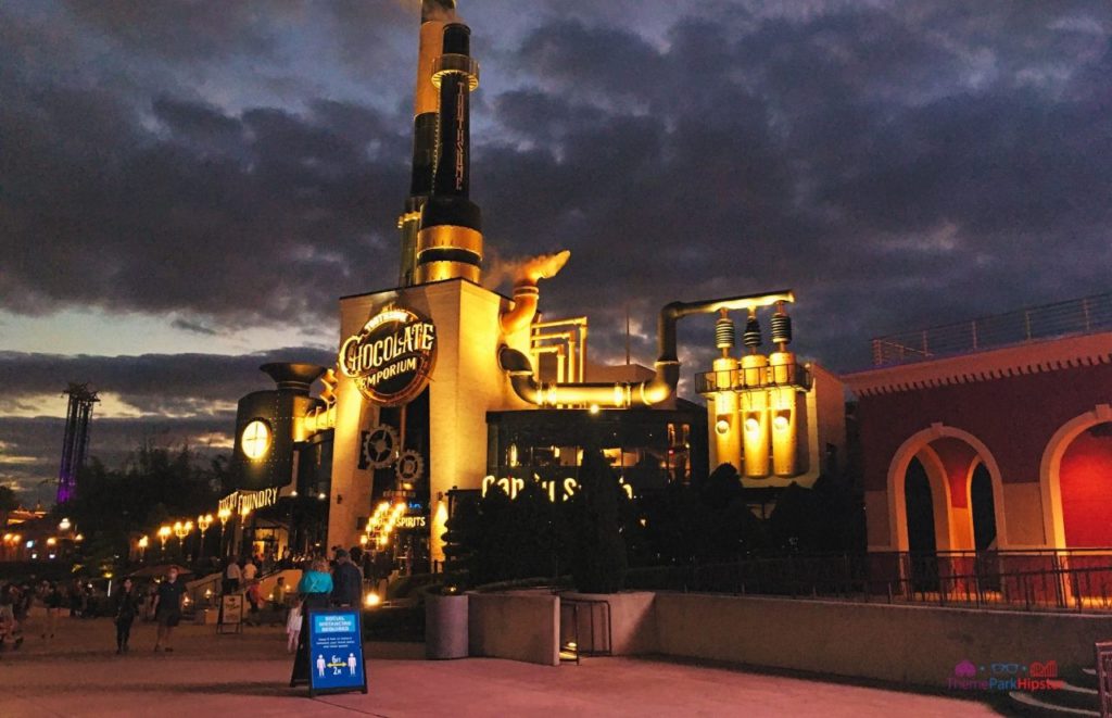 Nighttime outside the glowing Toothsome Chocolate Emporium with social distancing sign at the entrance. Keep reading to to find out more Mistakes to Avoid at Universal Orlando Resort!