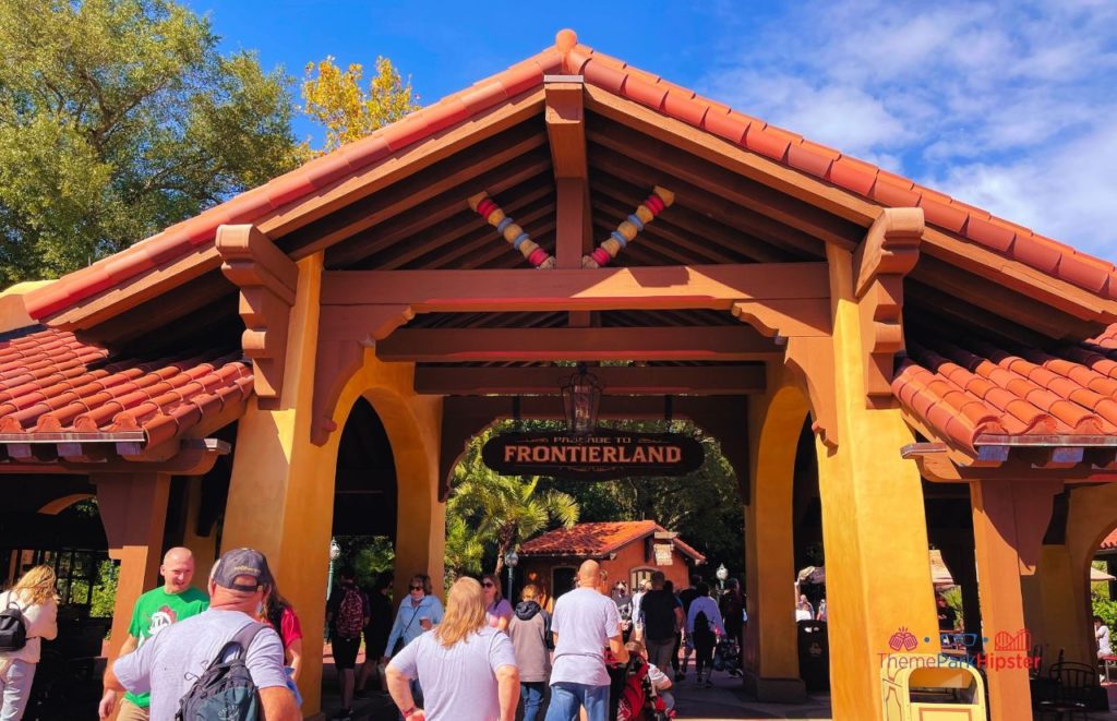 Disney Magic Kingdom covered entrance to Frontierland with guests walking under the Frontierland brown and yellow sign. Keep reading to discover more about the best place to watch Magic Kingdom fireworks.