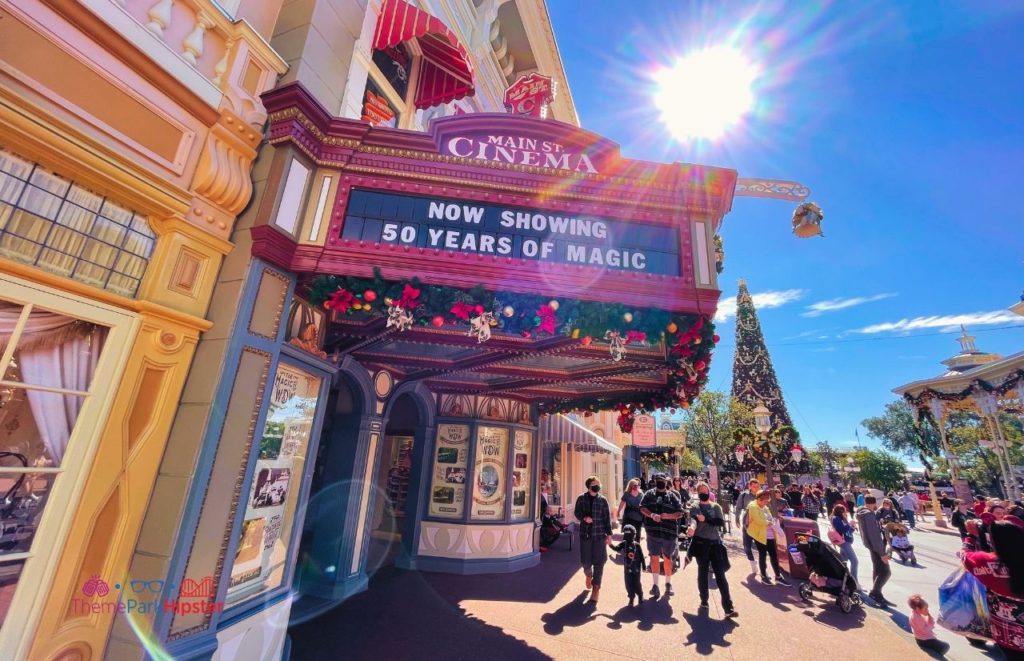 Disney Magic Kingdom Main Street Cinema with Christmas Tree in the Background. Keep reading to get the best Disney Christmas pictures and to know where to take the best Christmas photos at Disney World!