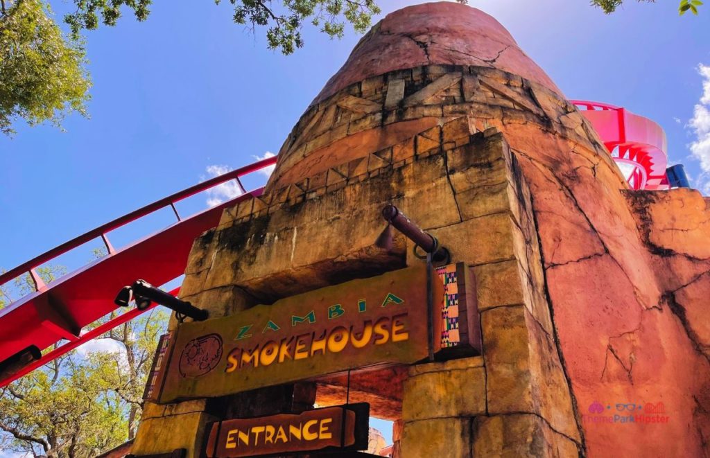 Busch Gardens Tampa Bay Zambia Smokehouse with an entrance  sign on an old looking rock formation  with carved blocks. Keep reading discover more about what to eat at Busch Gardens Tampa.