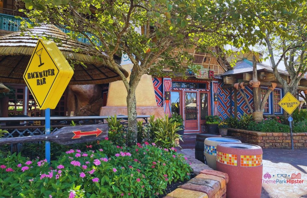 Universal Orlando Resort Patio area of Backwater Bar at Islands of Adventure with a yellow backwater bar crossing sign and lots of foliage. Keep reading to learn more about the best lounges at Universal Orlando. 