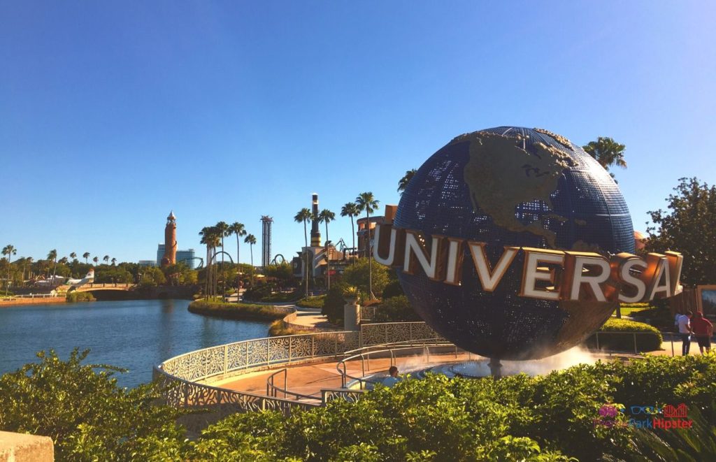 Universal Orlando Resort globe on citywalk with lighthouse from Islands of Adventure in the background. Keep reading to learn how to have the best Universal Orlando Solo Trip for Travelers going to theme parks alone.