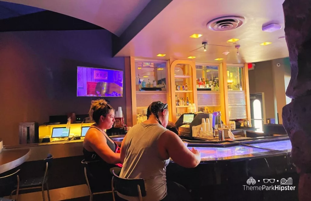 SeaWorld Orlando Resort Sharks Underwater Grill bar area with a full bar on display against the wall alongside a mounted television. Keep reading to learn more about Sharks Underwater Grill at SeaWorld Orlando.