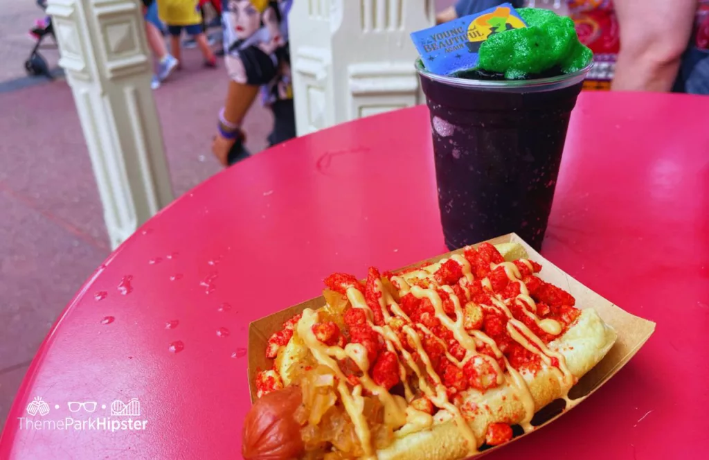 2023 Mickey's Not So Scary Halloween Party Food at Disney Magic Kingdom Theme Park Hocus Pocus Sanderson Sisters Black and Green Drink with Hotdog Topped with onions firehot cheetos and sauce at Casey's Corner
