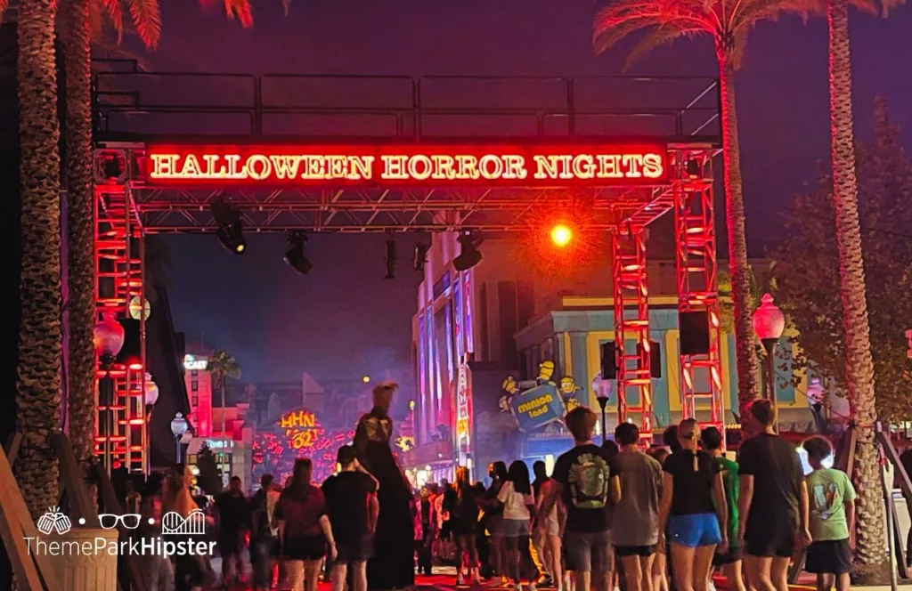 2023 Halloween Horror Nights HHN32 event sign glowing as theme park guests walk under it at Universal Studios Orlando. Keep reading to learn more about Universal Orlando Halloween Horror Nights Stay and Scream. 