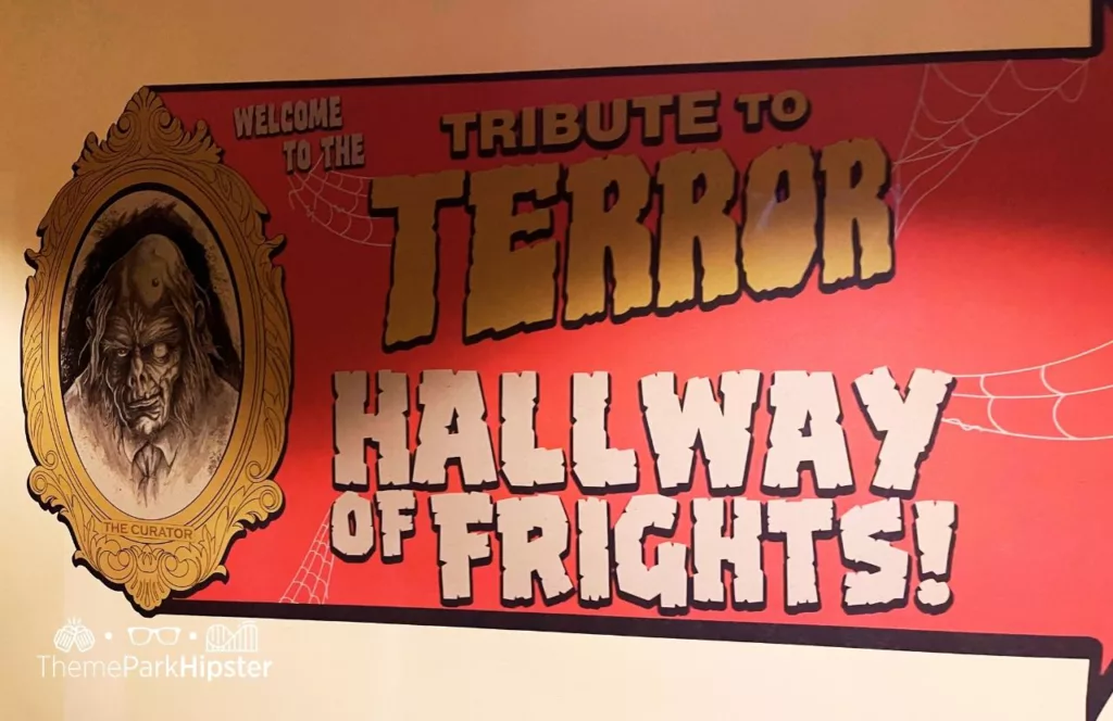 Spooky sign stating Welcome to the Tribute to Terror Hallway of Frights with a painting of a frightening face in a mirror at the 2023 Halloween Horror Nights HHN 32 at Universal Studios Orlando Comic Book Tribute Store. Keep reading to discover more about Halloween Horror Nights Stay and Scream.