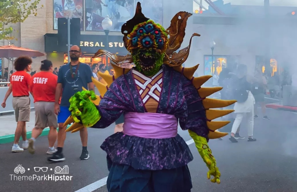 Oddfellow Carnival Scare Zone actor in festive and frightening purples and greens at 2023 Halloween Horror Nights HHN 32 Universal Studios Orlando.