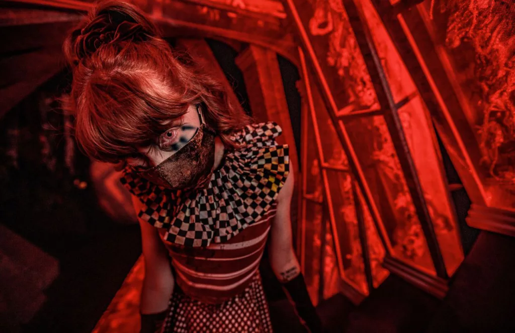 Mesmer Sideshow of the Mind haunted house with a scare actor ina  sideshow themed circus dress and mask at 2023 Knott's Scary Farm at Knott's Berry Farm in California. Keep reading to learn more about Knott’s Scary Farm haunted houses. 