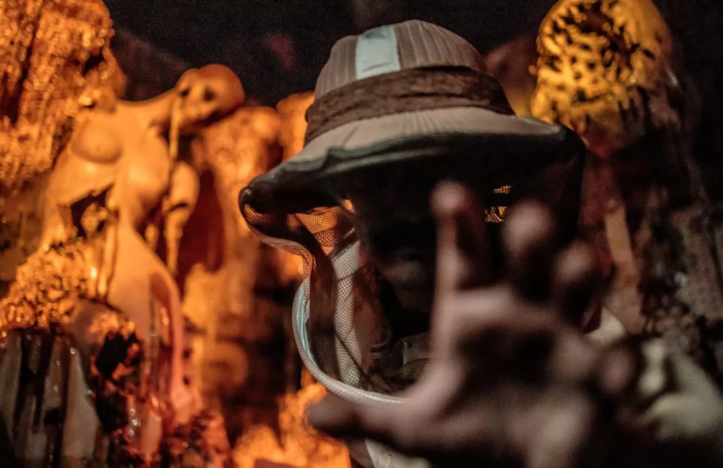 Character covered in protective netting and hat for beekeeping surrounded by molten wax melted characters behind at the Wax Works haunted house at the 2023 Knott's Scary Farm at Knott's Berry Farm in California. Keep reading to find out all there is know about Knott’s Scary Farm haunted houses. 