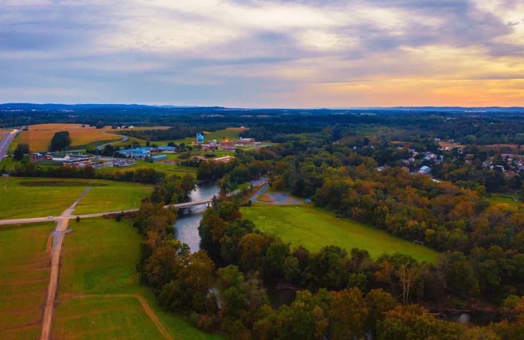 Aerial view of Swatara Creek Park near Hersheypark with big green fields, plenty of forests, the river creek and blue and orange vibrant skies. Keep reading to discover all the things to do close to Hersheypark