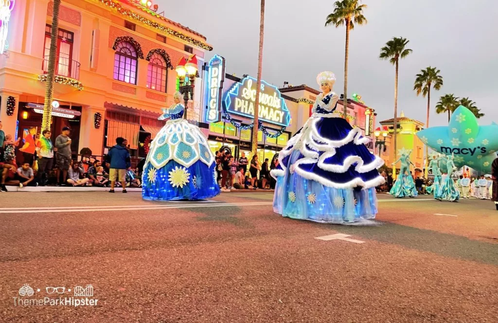 Christmas at Universal Orlando Macy's Holiday Parade featuring snowflake costumed characters on stilts and big blue gowns. Keep reading to discover more about Universal Studios Christmas Parade. 