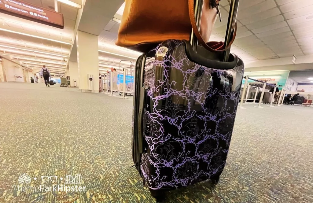 Disney Villains Purple and Black suitcase in the airport. Keep reading to learn how to pack for your solo theme park trip.